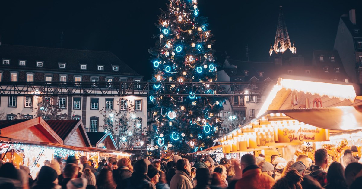 Christmas tree, glowing market stalls and visitors in Strasbourg at night